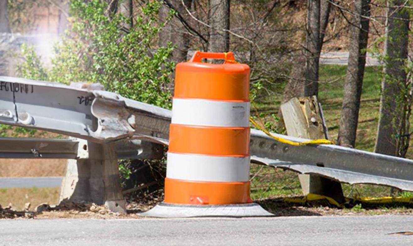 Damaged roadside guardrail marked with a safety barrel, representing fixed property claims.