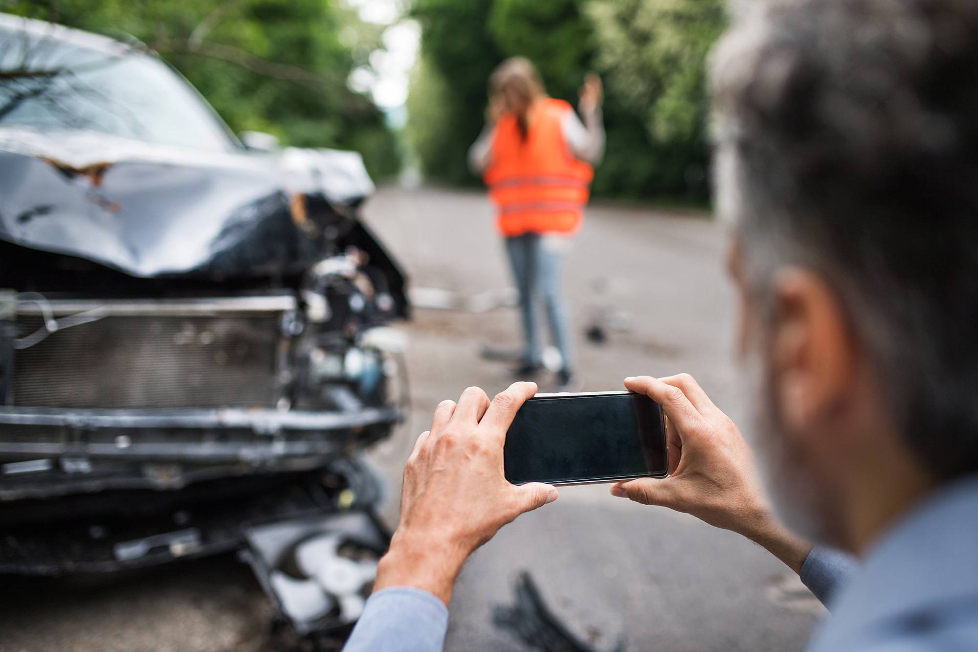 Person photographing car accident damage with a smartphone at the scene.