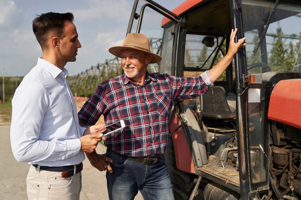 Adjuster evaluating specialty farm equipment with a farmer beside a tractor.